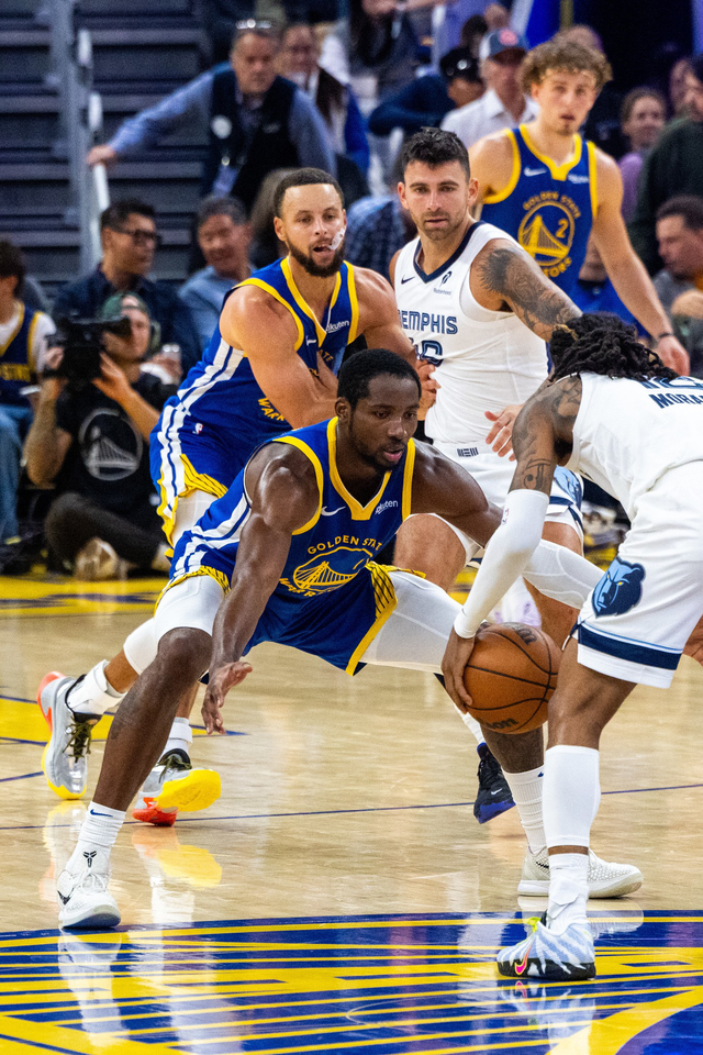 Two Golden State Warriors players and two Memphis Grizzlies players compete intensely for the basketball on the court during a game.
